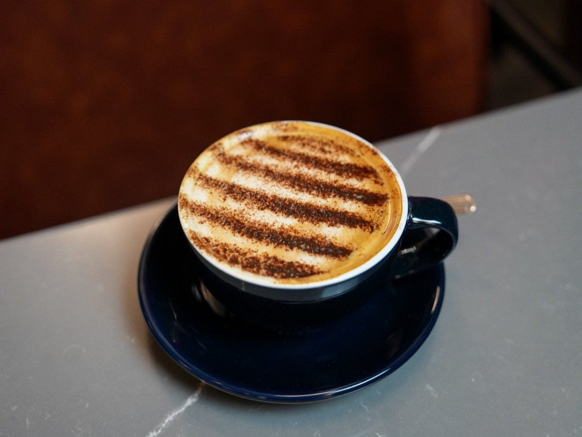 Cappuccino dusted with chocolate stripes on a marble table at Canons Cafe, Edgware