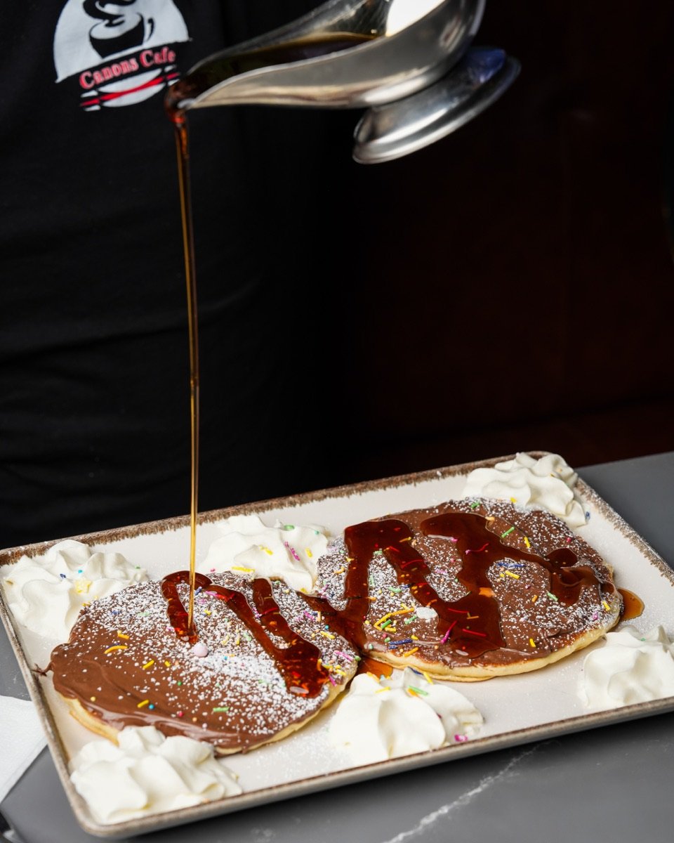Chocolate and strawberry pancakes with syrup being poured at Canons Cafe, Edgware