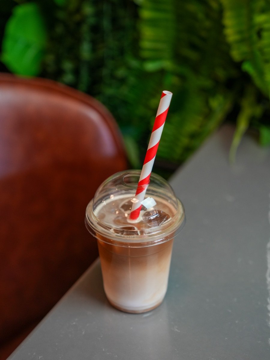 Iced latte in a takeaway cup with a striped paper straw at Canons Cafe near Canons Park station