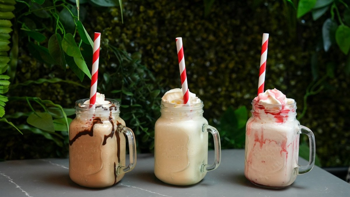 Chocolate, vanilla and strawberry milkshakes in mason jars against a green wall at Canons Cafe, Edgware