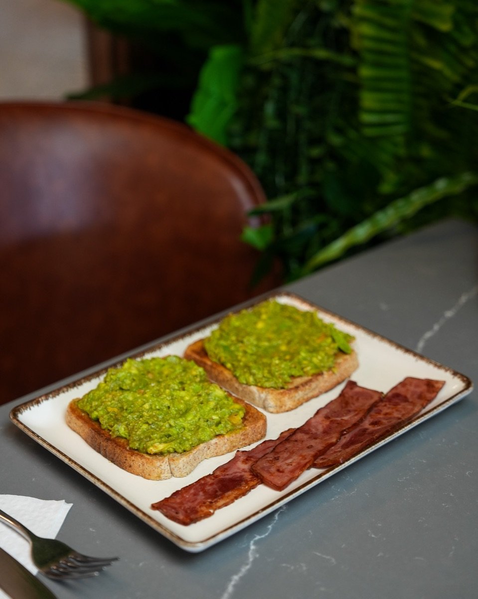 Two slices of smashed avocado on toast with turkey bacon on a stone table at Canons Cafe near Canons Park station